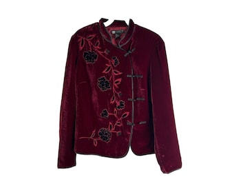 May include: A burgundy velvet jacket with black floral embroidery and a mandarin collar. The jacket has a front closure with black buttons.