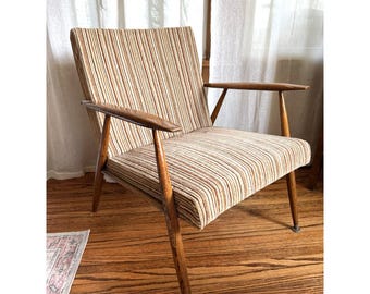 May include: An armchair featuring a wooden frame with tapered legs and flat armrests. The seat and backrest are upholstered in a fabric with a vertical striped pattern in shades of brown, tan, cream, and black, creating a textured appearance.