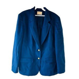 Op de afbeelding: Een donkerblauwe blazer met gouden knopen. De blazer heeft een klassieke stijl en is gemaakt van een gladde stof.