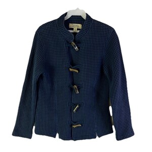 May include: A navy blue waffle-knit jacket with a mandarin collar and wooden toggle closures. The jacket has long sleeves and a textured appearance. The brand label is visible at the neckline. The jacket is hanging on a white hanger.