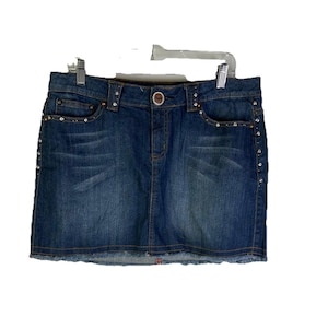 May include: A blue denim skirt with a classic five-pocket design. The skirt features decorative rhinestones along the pockets and sides, and a button closure. The hem is frayed.
