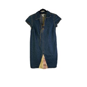 May include: A short-sleeved denim dress with a collared neckline and a lace-up front. The dress features a knee-length skirt with a decorative panel at the hem. The dress is a medium wash blue denim.