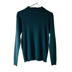 Puede incluir: Un suéter de color verde oscuro de punto de canalé con cuello alto y mangas largas.