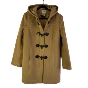 May include: A tan duffle coat with a hood and toggle closures. The coat has a classic design with a tailored fit. The hood is lined with a lighter-colored fabric. The coat is hanging on a black hanger.