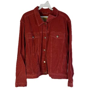 Puede incluir: Chaqueta de pana roja con cierre de botones, dos bolsillos en el pecho y dos bolsillos laterales. La chaqueta está colgada de una percha blanca. La chaqueta tiene cuello y mangas largas.
