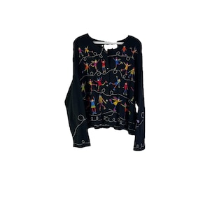May include: Black cardigan sweater with colorful embroidered figures in various poses. The long-sleeved sweater has a button-up front and a round neckline. The figures are in red, yellow, blue, and green.