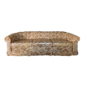 May include: A vintage sofa with a three-cushion design. The sofa features a gold and white paisley pattern fabric. The arms and back are rounded, and the base has a skirt. A classic piece of furniture.