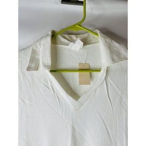 May include: White collared shirt with a v-neck and a small tag hanging from the collar.