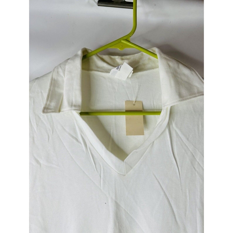 May include: White collared shirt with a v-neck and a small tag hanging from the collar.