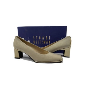 May include: A pair of beige pumps with gold heels. The shoes are made by Stuart Weitzman.