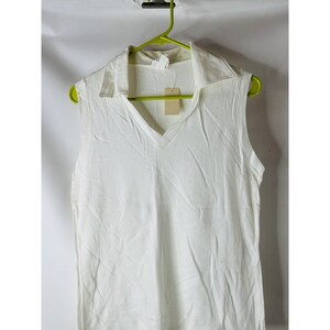 May include: A white sleeveless shirt with a v-neck and a collar. The shirt is hanging on a green hanger.