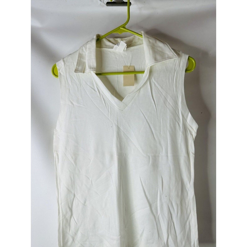 May include: A white sleeveless shirt with a v-neck and a collar. The shirt is hanging on a green hanger.