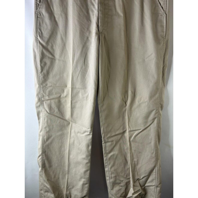 May include: A pair of beige casual trousers. The trousers have a straight leg and a relaxed fit.