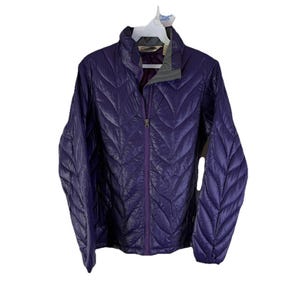 Könnte beinhalten: Tiefviolette Steppjacke mit durchgehendem Reißverschluss und Stehkragen. Die Jacke hat ein Zickzackmuster und hängt an einem weißen Kleiderbügel. Das Innenfutter ist dunkelviolett.