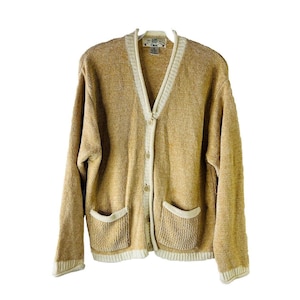 May include: A tan cardigan with a white trim around the collar, pockets, and bottom hem. The cardigan has a button closure and a v-neck.