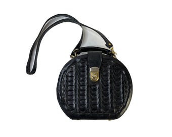 May include: A black leather round handbag with a woven pattern and a gold clasp. The bag has a long strap for carrying it on the shoulder.