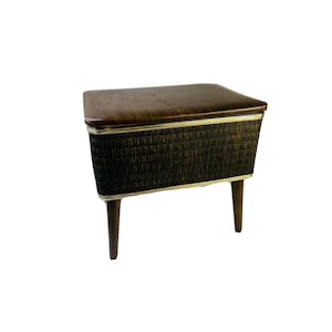 May include: A vintage sewing box with a dark brown wooden top and legs. The sides are a textured black material with gold trim. The sewing box is rectangular and has a hinged lid.