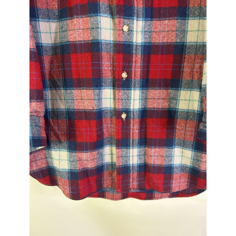 May include: A red, blue, and white plaid button-up shirt. The shirt features a classic plaid pattern with a mix of red, blue, and white squares. It has a collared neckline and button closures down the front. The shirt is made of a soft, textured fabric.