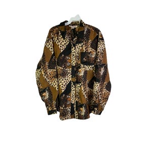 May include: A long-sleeved button-down shirt with a leopard print pattern in shades of brown, black, and tan. The shirt has a collared neckline and a single pocket on the chest. The fabric appears to be a silky material.