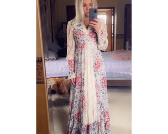 Puede incluir: Un vestido largo blanco maxi con estampado floral en tonos rojos, azules y blancos. El vestido tiene una superposición de encaje y mangas largas.