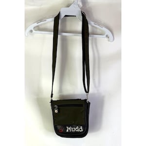 May include: Olive green Mudd crossbody bag with a black strap and silver hardware. The bag has a front flap with the Mudd logo in white and a red heart. The bag is hanging on a white hanger.