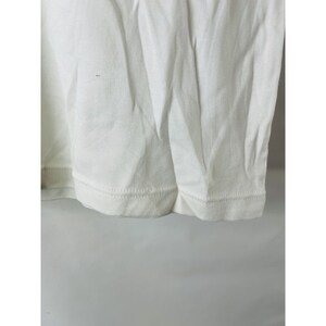 May include: Close-up of the bottom hem of a white t-shirt. The hem is stitched with a straight stitch.