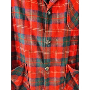 May include: A red, green, and blue plaid flannel shirt with a button-up front and two pockets. The shirt has a classic, vintage look.