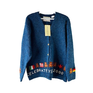 May include: A blue cardigan with a V-neck and button fastening. It has embroidered teddy bears and flags, with the text "CELEBRATE EYE 2000". A tag is attached to the neckline. The sweater is a vintage item.