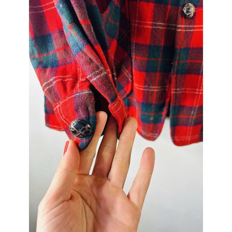 May include: Red and green plaid flannel shirt with a button closure and a black button on the cuff.