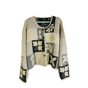 Könnte beinhalten: Ein beiger Cardigan mit einem schwarzen und cremefarbenen Blumendesign. Der Cardigan hat einen Knopfverschluss und lange Ärmel.