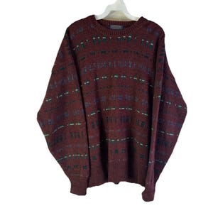 May include: A burgundy sweater with a crew neck and long sleeves. The sweater features a pattern of horizontal and vertical lines in shades of green, blue, and brown. The sweater is hanging on a white hanger.