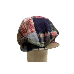 May include: A patchwork style newsboy cap with a blue, red, and white plaid pattern. The cap has a slightly curved brim and a rounded crown.