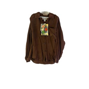 May include: A long-sleeved brown shirt with a collar and button-down front. A tag with floral imagery hangs from the shirt. The shirt is made of a soft, flowing fabric.