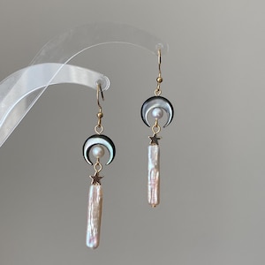May include: Gold-tone earrings with a crescent moon design and a pearl centre. Below the moon is a gold star and a long, off-white, pearl-like bead. The earrings hang from gold-tone ear wires.