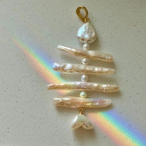 May include: A pendant necklace with a gold-coloured clasp and a series of natural, irregularly shaped pearls. The pearls are in varying sizes and shapes, with a pearlescent sheen. The design is vertical, with the pearls strung together.