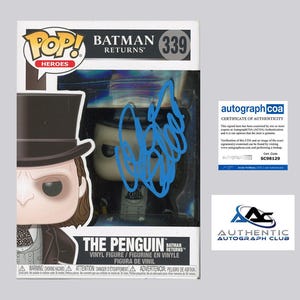 Może przedstawiać: Figurka winylowa Funko Pop! Pingwina z filmu Powrót Batmana. Figurka jest w oryginalnym opakowaniu i ma niebieski autograf. Pudełko ma numer 339 i napis "POP! Heroes". Zawiera certyfikat autentyczności Authentic Autograph Club.
