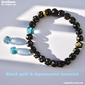 May include: Black beaded bracelet with a gold charm and aquamarine beads. The bracelet is on a white surface. "Black gold & Aquamarine bracelet" is written below the bracelet. "unigeml.etsy.com" is written in the bottom right corner.