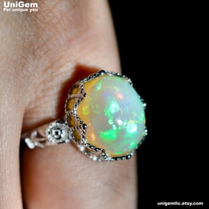 May include: A silver ring featuring a large, round, cabochon-cut opal gemstone with vibrant green and orange flashes of color. The setting has an intricate, openwork metal design with a textured, beaded edge surrounding the central stone.