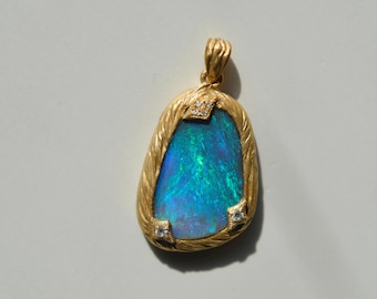 May include: A gold pendant with an oval, iridescent blue-green opal stone. The pendant has a textured gold frame with small diamonds at the top and bottom corners. The pendant is suspended from a textured gold bail.