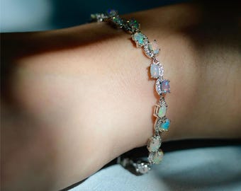 May include: A silver bracelet with a row of oval-shaped opal gemstones set in a silver chain. The bracelet is on a person's wrist.