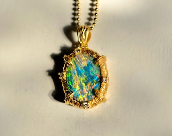 May include: A gold pendant necklace featuring an oval-shaped opal with vibrant blue, green, and orange flashes. The opal is set in a textured gold frame with four small accent stones at the prongs, suspended from a gold ball chain necklace.