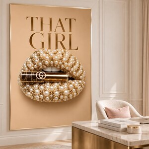 May include: A rectangular wall art print featuring a beige background with the text THAT GIRL in large dark letters. Centered is a graphic of lips covered in white pearls and gold beads, holding a gold lipstick tube with a double G logo.