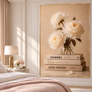 May include: A large framed wall art print featuring a glass vase filled with three cream-colored peony flowers resting on a stack of three beige books labeled Chanel, Dior, and Louis Vuitton, set against a soft, neutral-toned background.