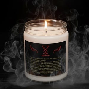 May include: A lit white candle in a glass jar with a black label featuring the word "LUCIFER" and a red emblem. The candle is surrounded by wisps of smoke against a dark background.