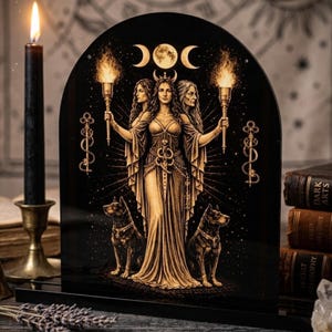 Op de afbeelding: Zwart en goud decoratief paneel met een centrale figuur die fakkels vasthoudt, geflankeerd door honden. Het paneel heeft een halve maan ontwerp. Een zwarte kaars en boeken zijn op de achtergrond.