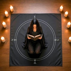 Pode incluir: Uma toalha de altar quadrada preta com um design de bússola circular branca com os pontos cardeais N, E, S e O impressos nas bordas. A toalha é cercada por oito velas de pilar brancas acesas dispostas em círculo num chão de madeira.