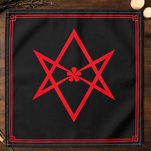 May include: A square black fabric cloth featuring a bold red geometric star symbol at the centre. The star is composed of two overlapping triangles with a small five-petaled flower shape in the middle. A double red border frames the entire edge.