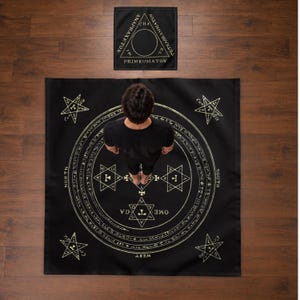 May include: A black square mat and a smaller matching square cloth featuring gold occult symbols, including a central circle with Hebrew text, four corner pentagrams, and the words North, South, East, and West. The top cloth displays a triangle.