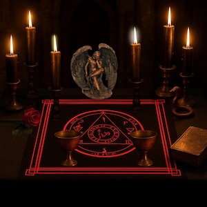 May include: A dark, moody scene featuring a black altar cloth with a red geometric design and symbols. Lit candles in ornate holders surround a statue of two figures with wings. Two chalices and a book are also present.