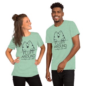 May include: Two people wearing light green t-shirts with a black and white cartoon cat graphic. The text on the shirt says "Fluff Around and find out!"